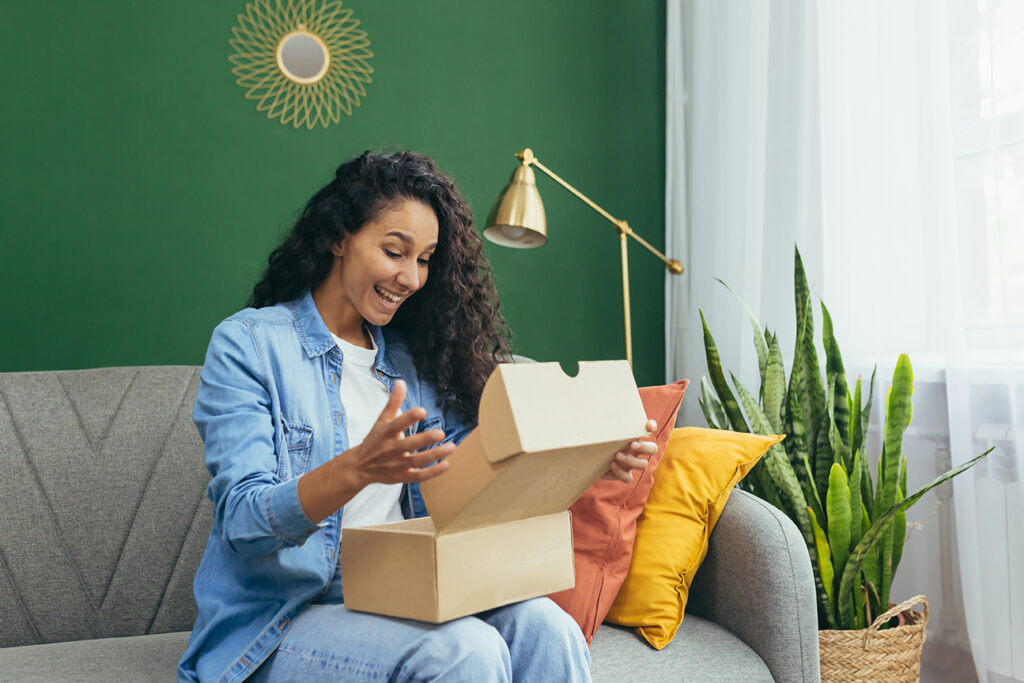 Mulher abrindo uma caixa com brindes e produtos personalizados em casa
