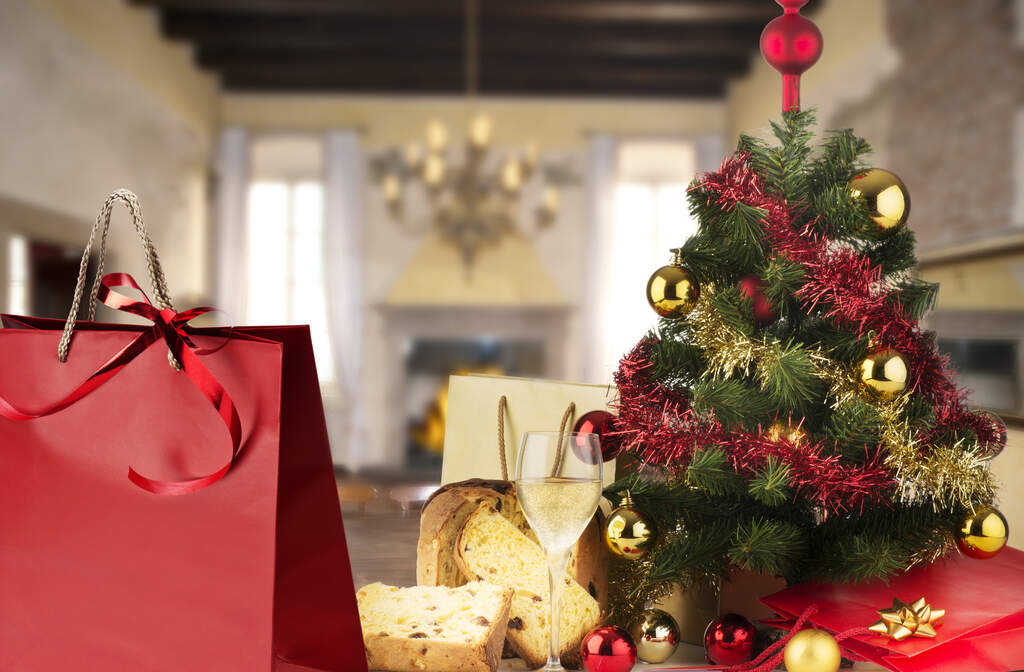 árvore de natal decorada em vermelho e dourado ao lado de uma sacola vermelha como brindes de natal para clientes.