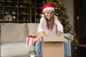 mulher usando um chapéu de natal abrindo uma caixa com brindes de natal
