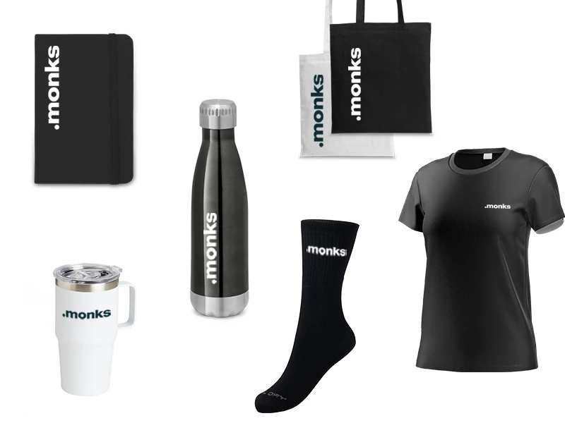 Imagem contendo produtos da marca Monks, como cadernos, garrafas, canecas, sacolas, camisetas e meias, todos com o logo .monks.