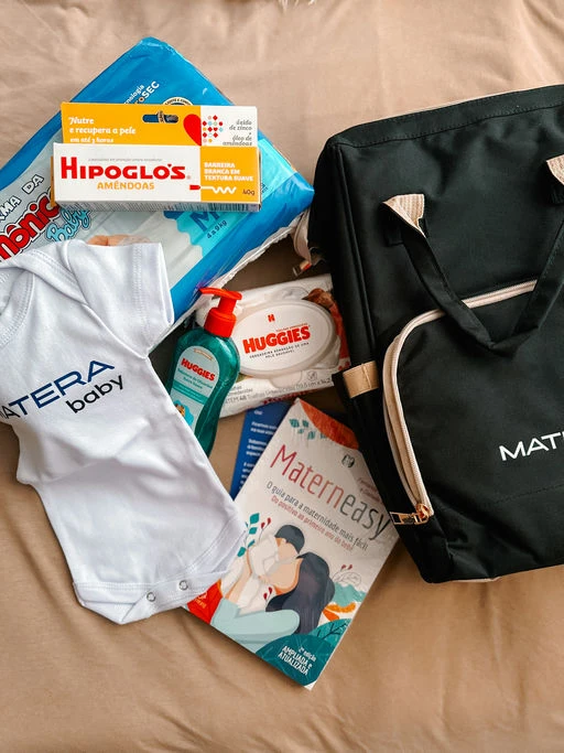 Imagem de produtos essenciais para bebês, incluindo fraldas, lenços umedecidos, creme para assadura e um body da Matera Baby, ideal para cuidados infantis.